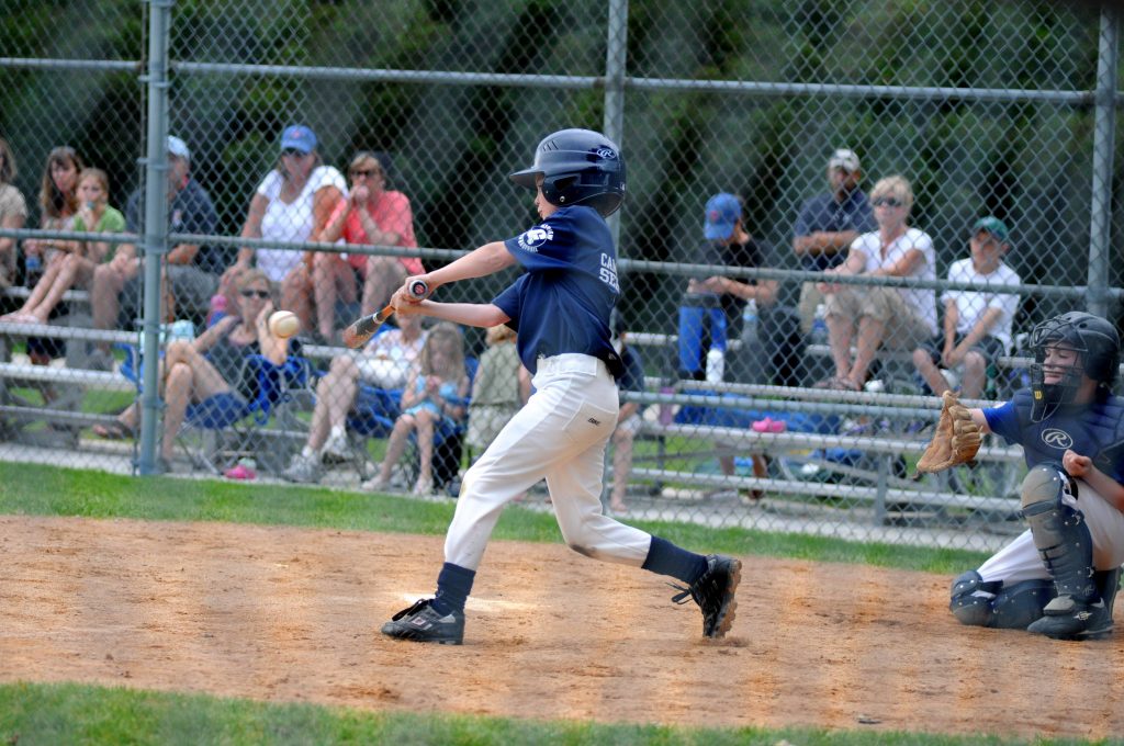 Encouraged Kindergartner hitting a strong baseball shot with a baseball in hand.