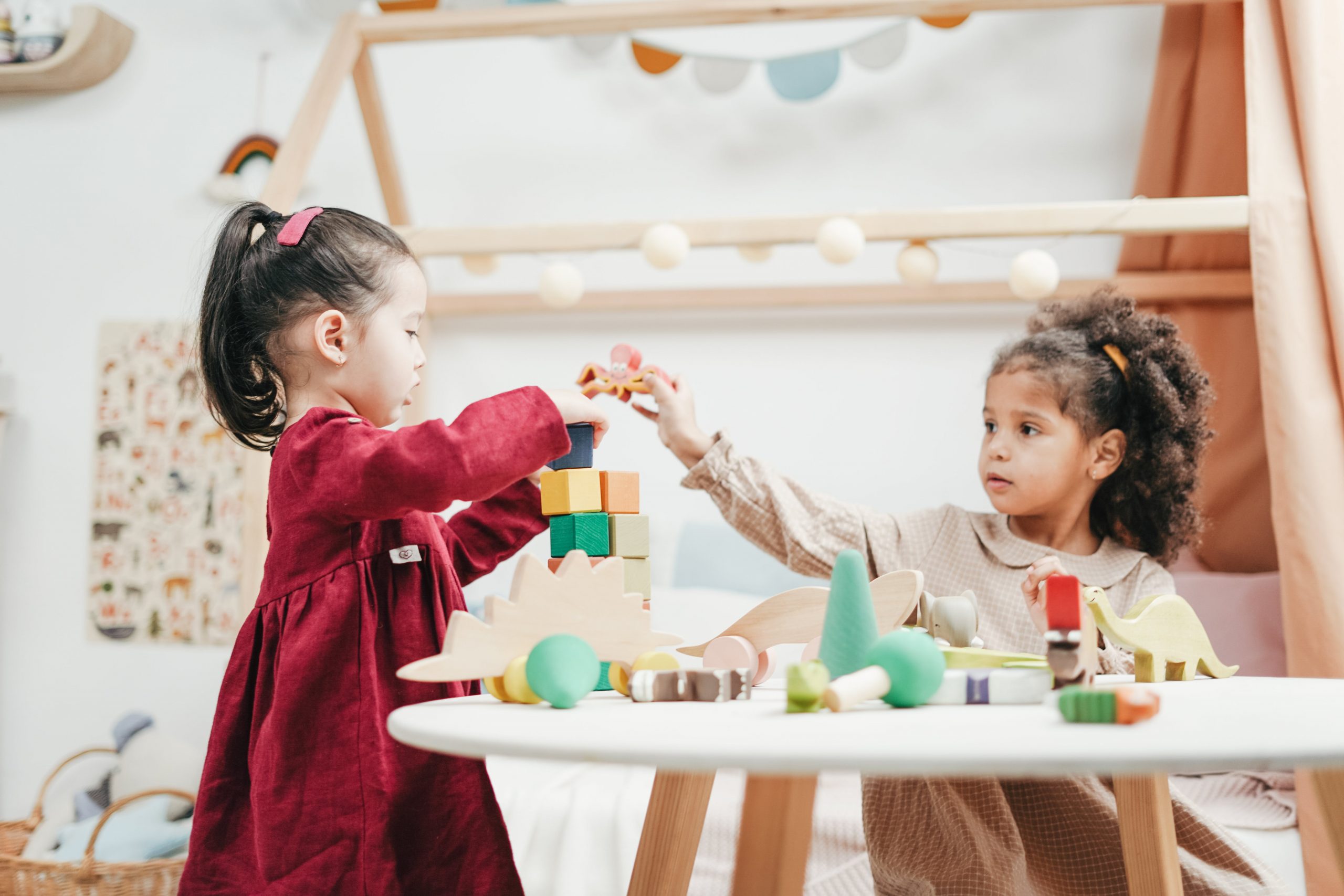 Two children playfully interact with colorful blocks and toys on a table in a playroom.
