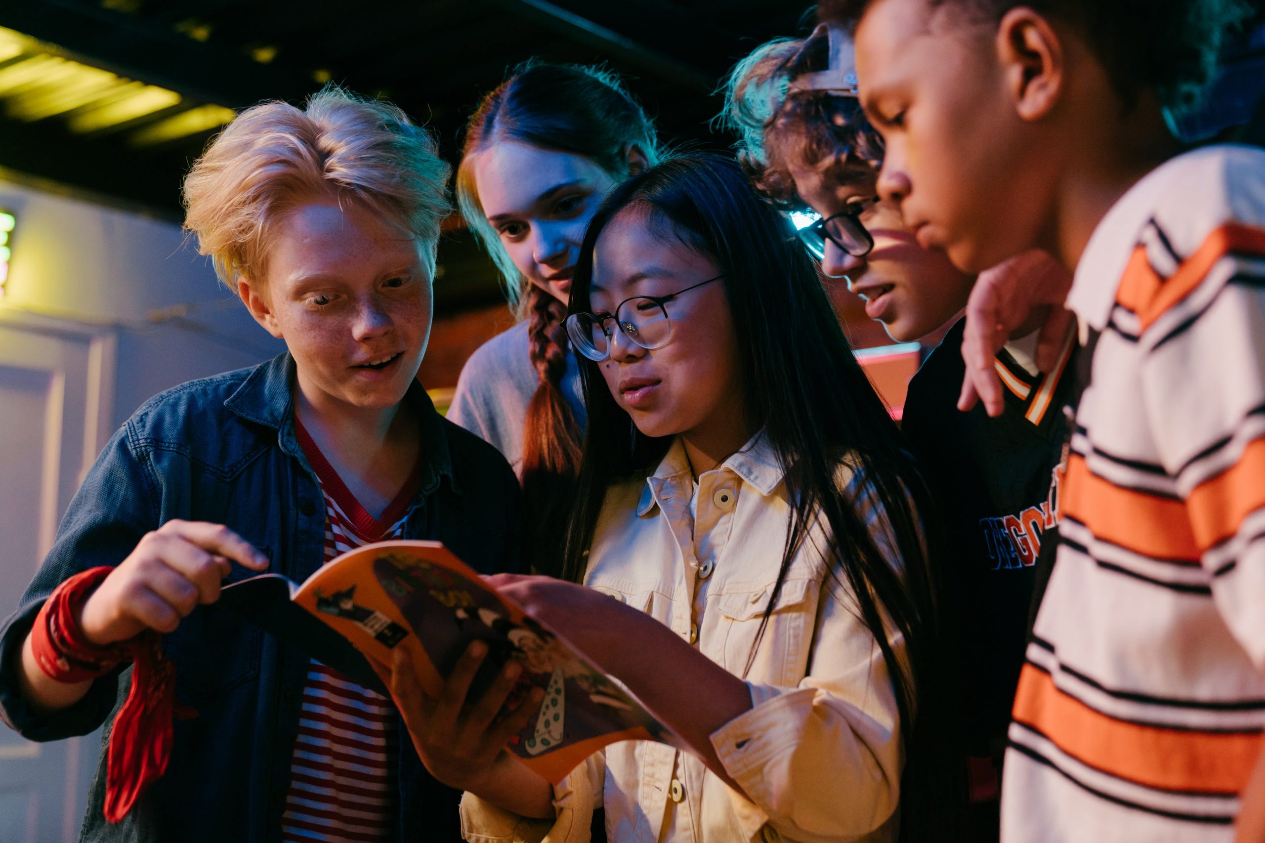 A diverse group of teenagers engaged in reading a comic book together in colorful lighting. 
