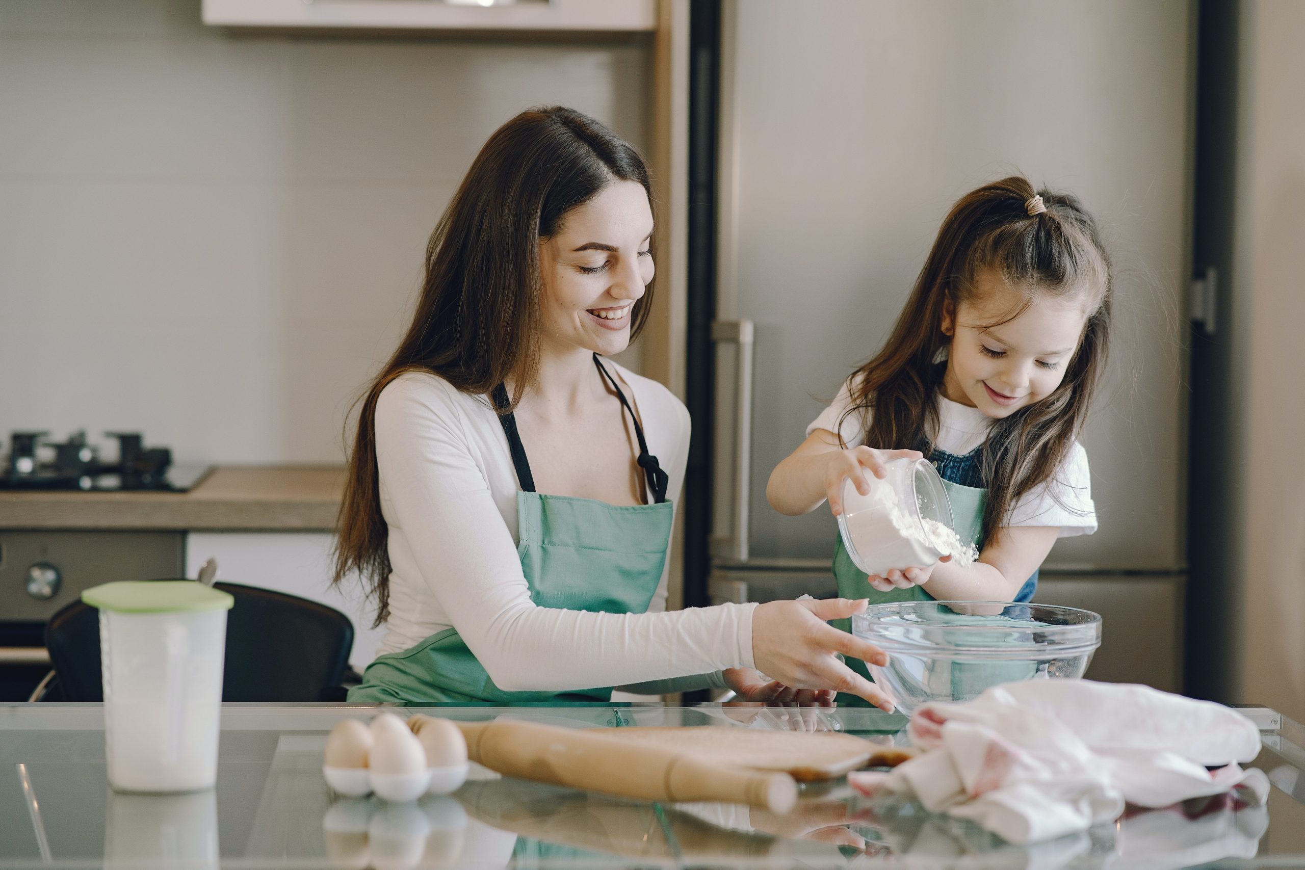 A girl is helping her mother bake a cake in the kitchen