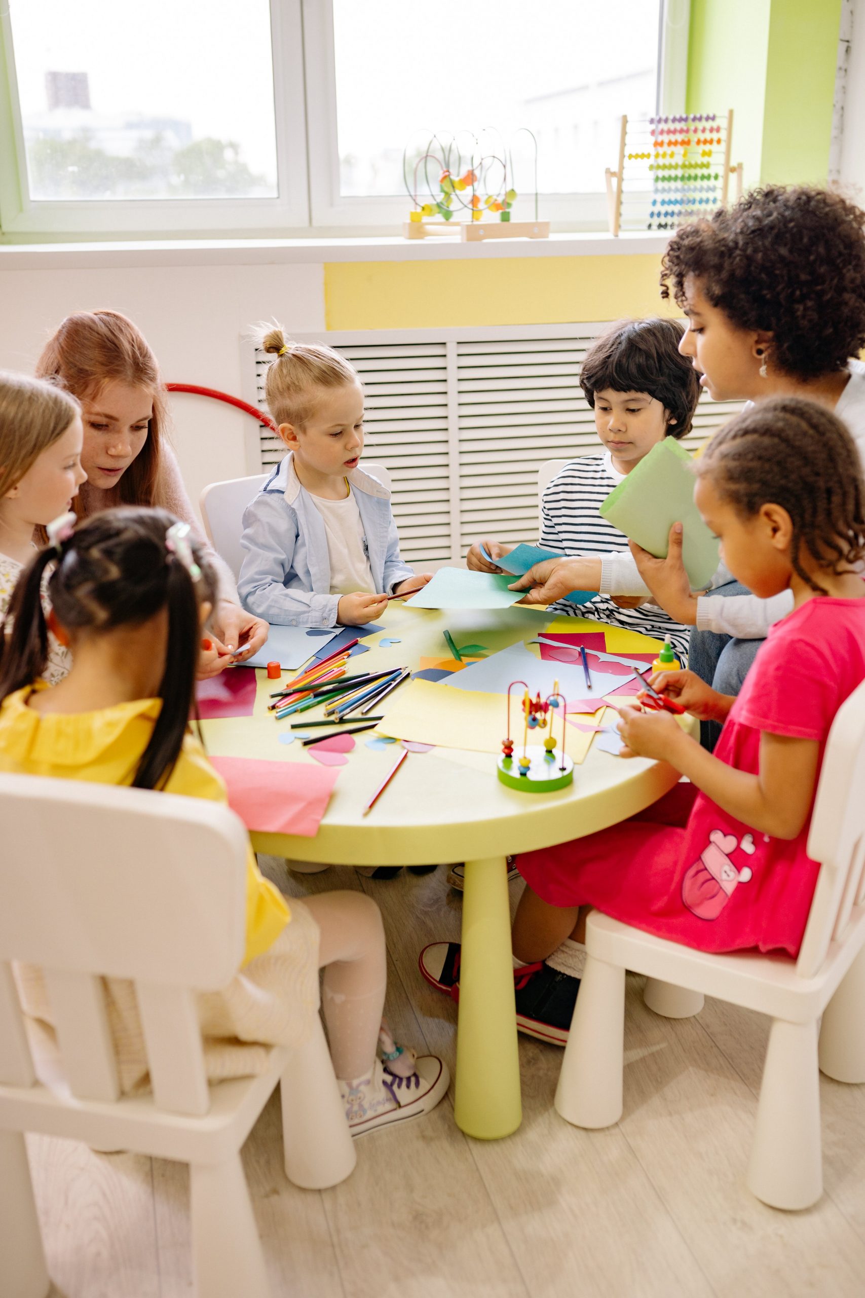 Diverse group of children engaged in creative play with paper and crayons at a table. 