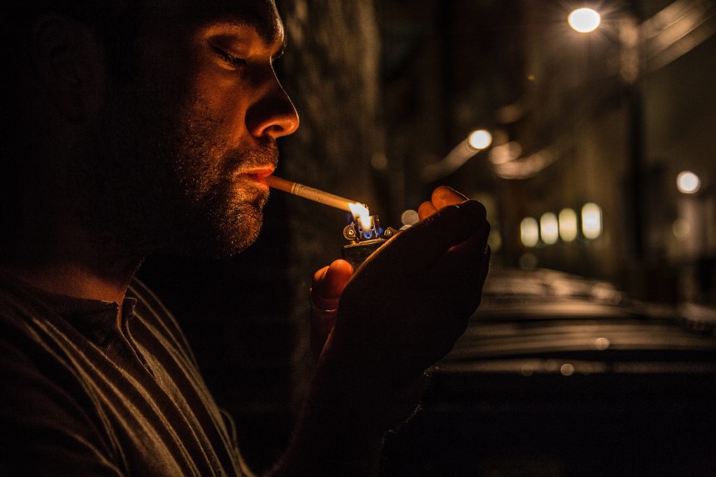 A Man smoking a Cigarette outside his house.