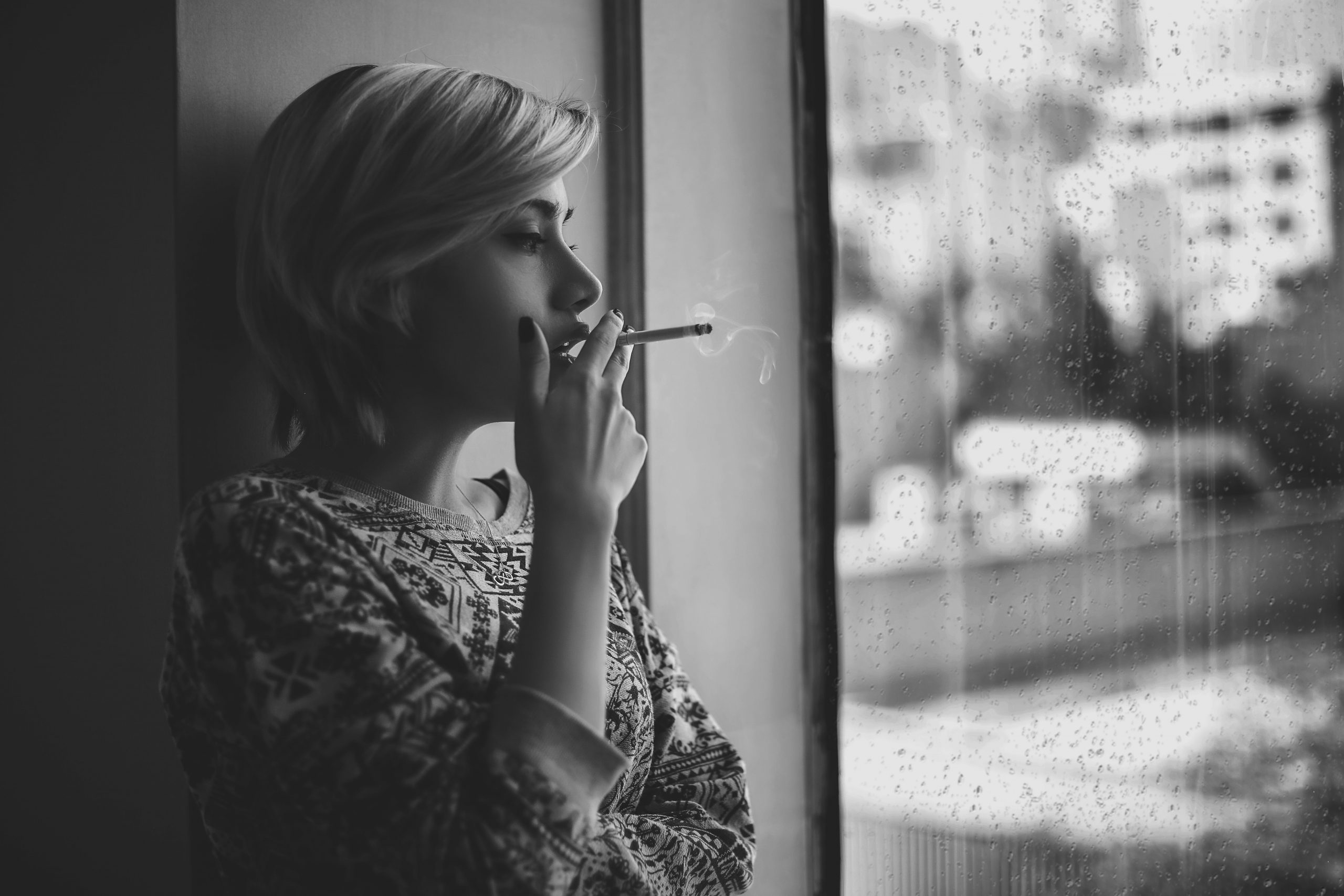 A girl is standing by the window smoking a cigarette