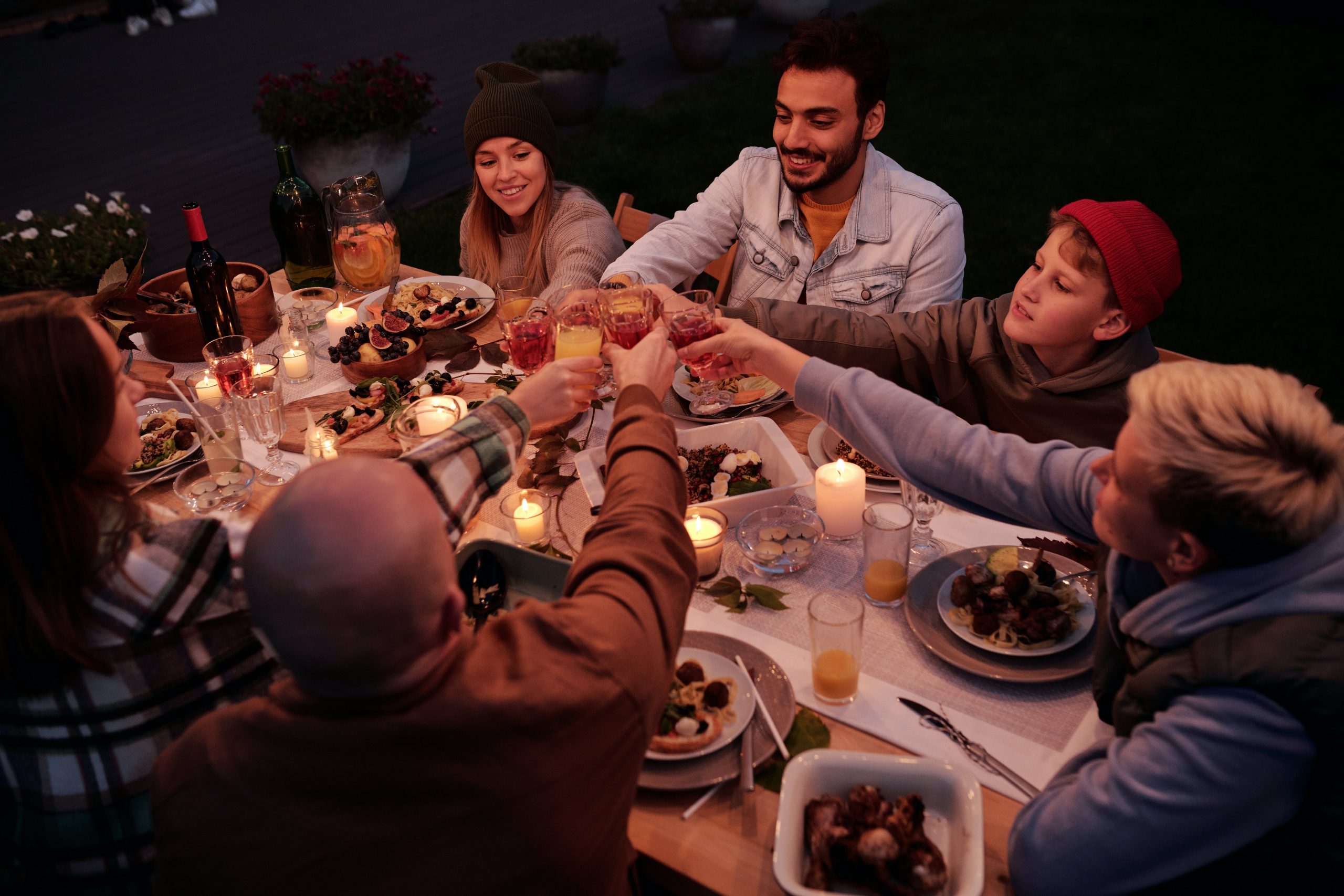A group of people enjoying an outdoor dinner party with candles and toasting drinks.