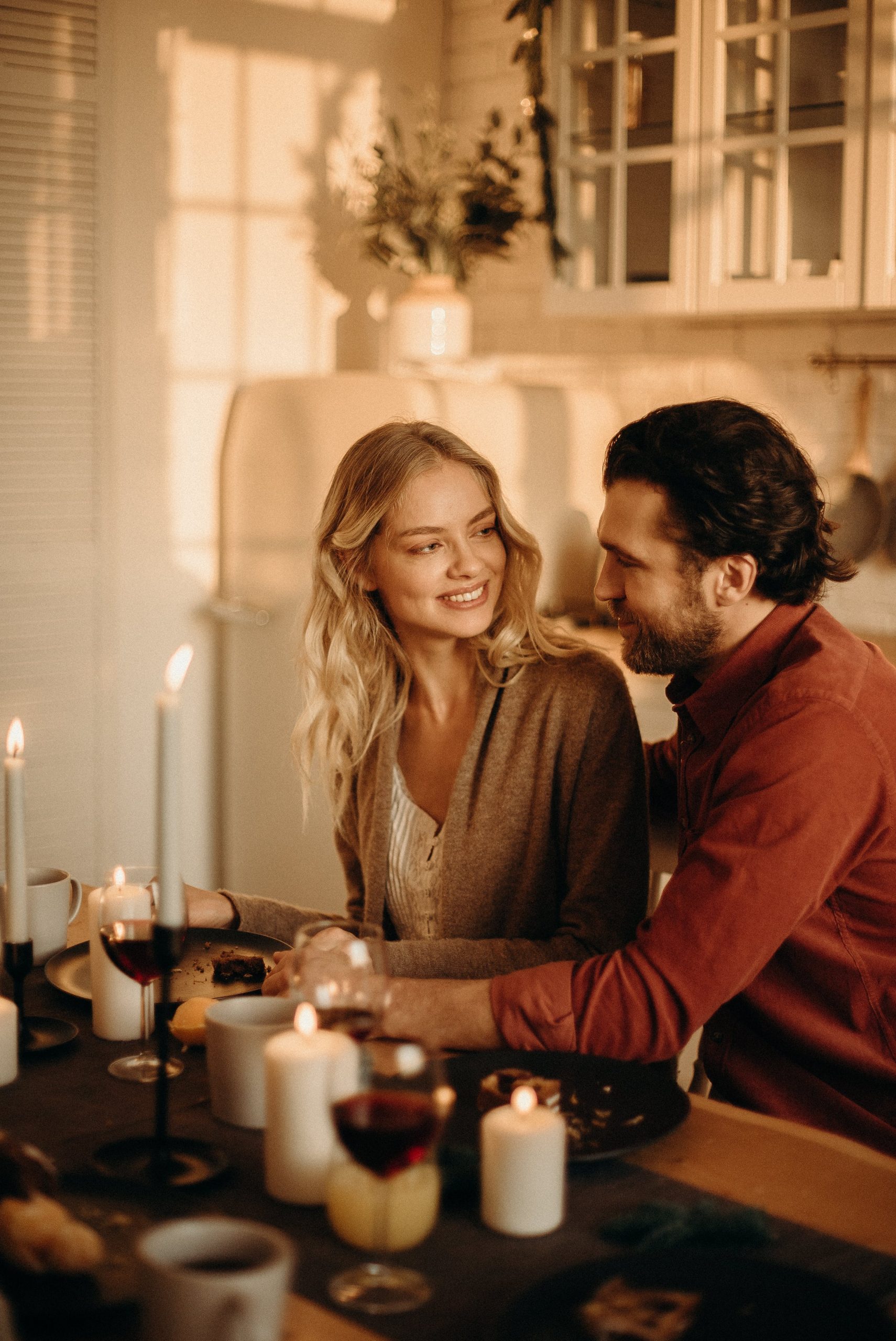 A cozy candlelit dinner with a smiling couple gazing at each other over wine glasses.