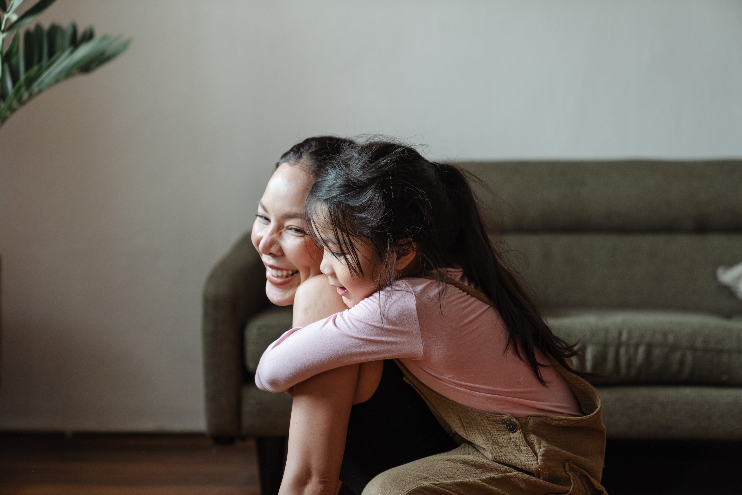 A joyful woman and a young girl hugging and laughing together in a cozy home setting.