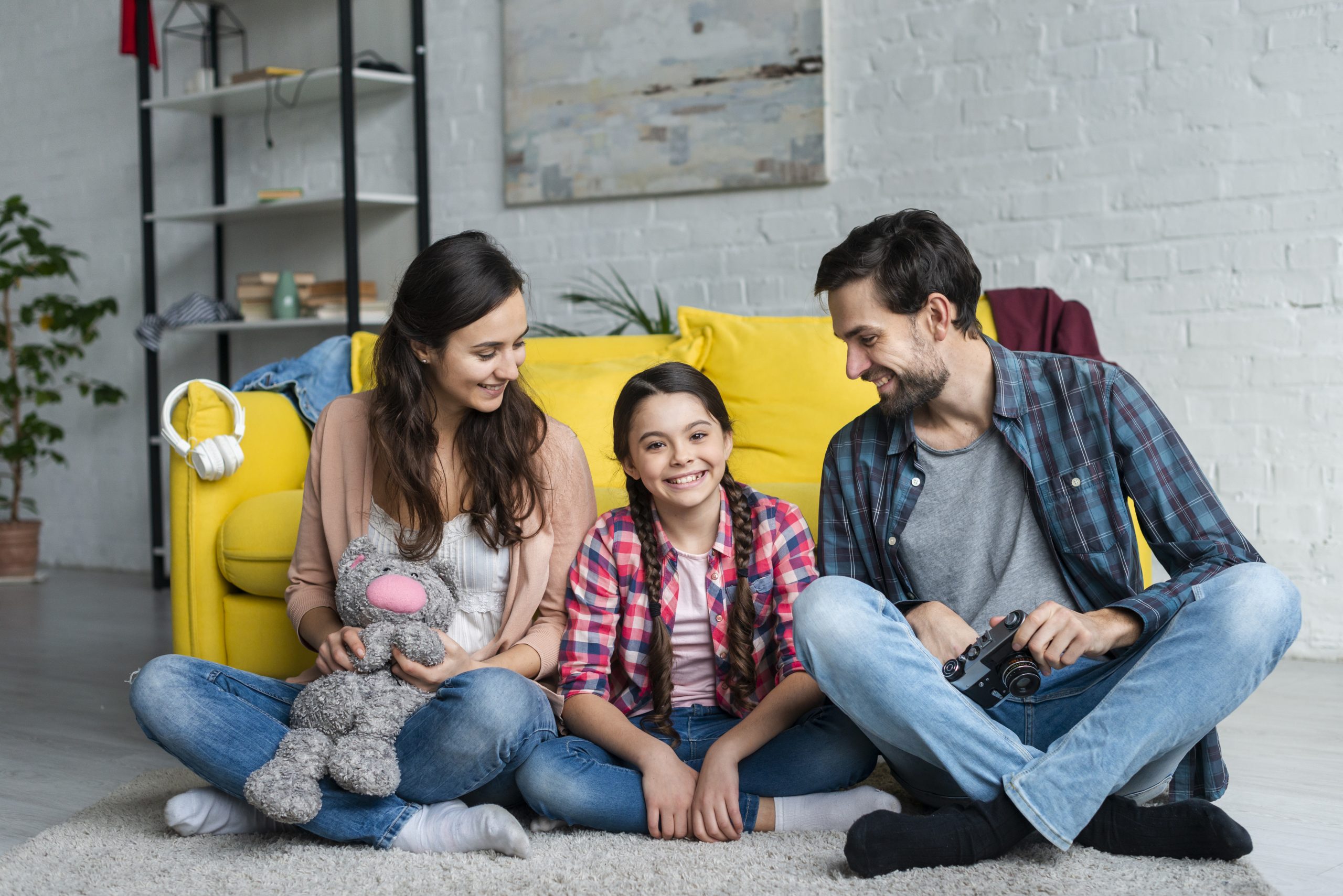 A family with a young girl sitting on the floor, smiling and holding a camera. 