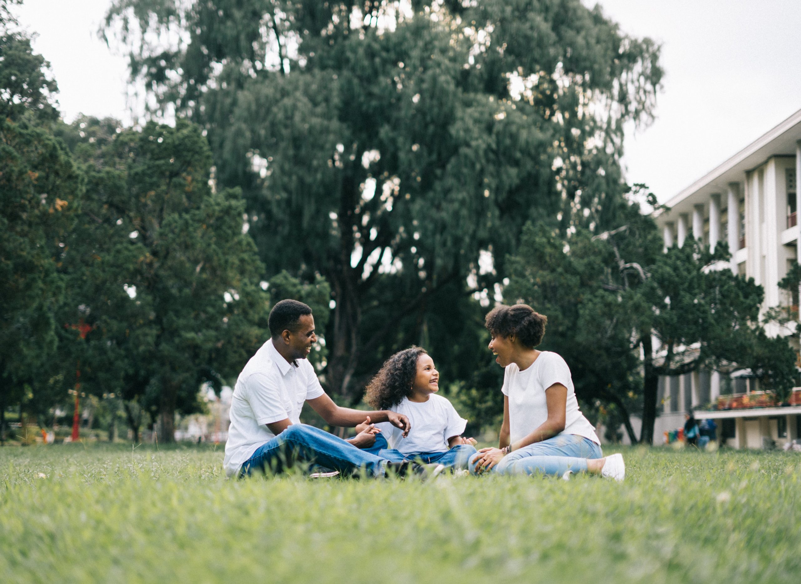 A joyful family sitting on grass in a park, parents and child laughing together. 
