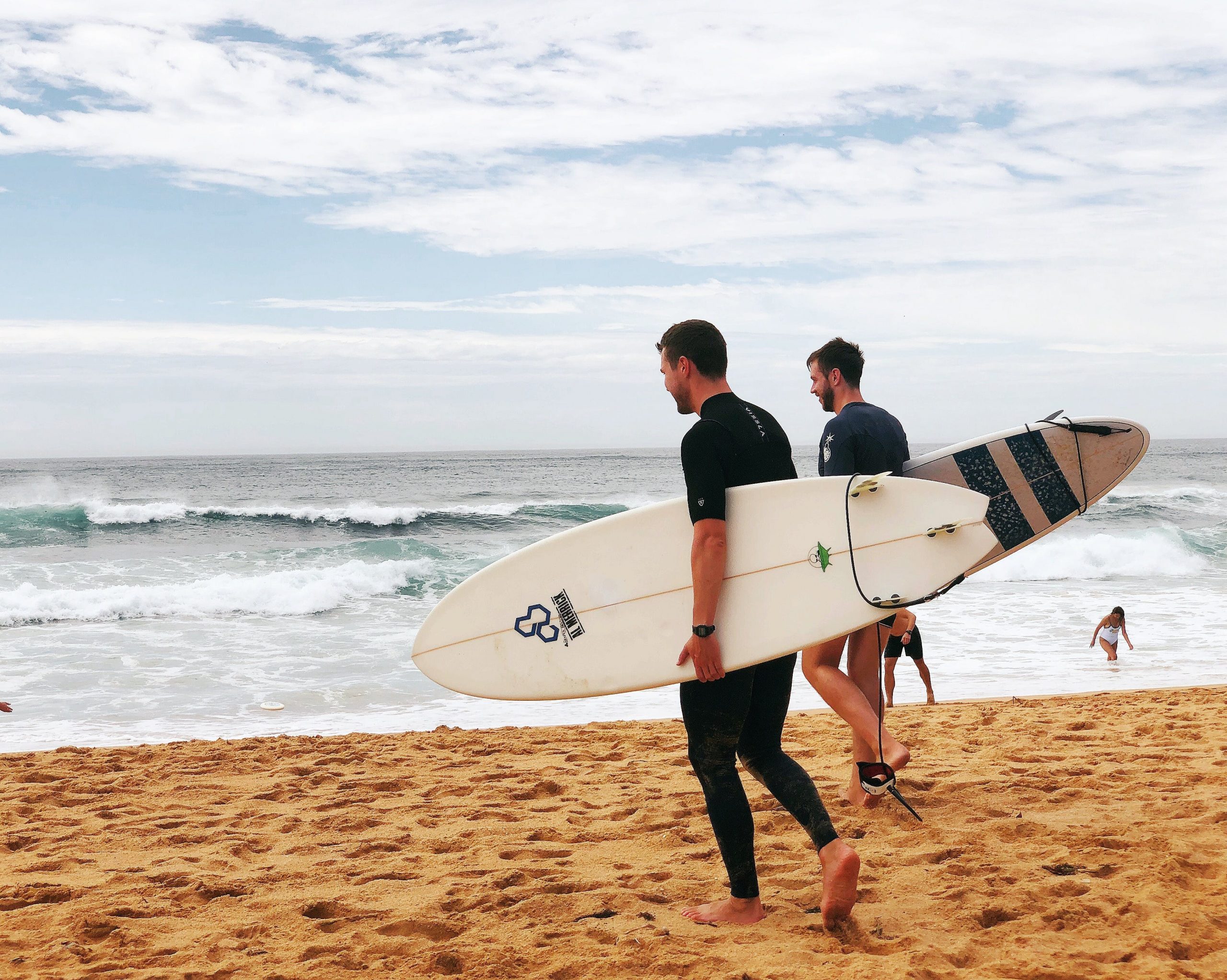 Two surfers walking on the beach with surfboards, ready to enter the ocean waves. 