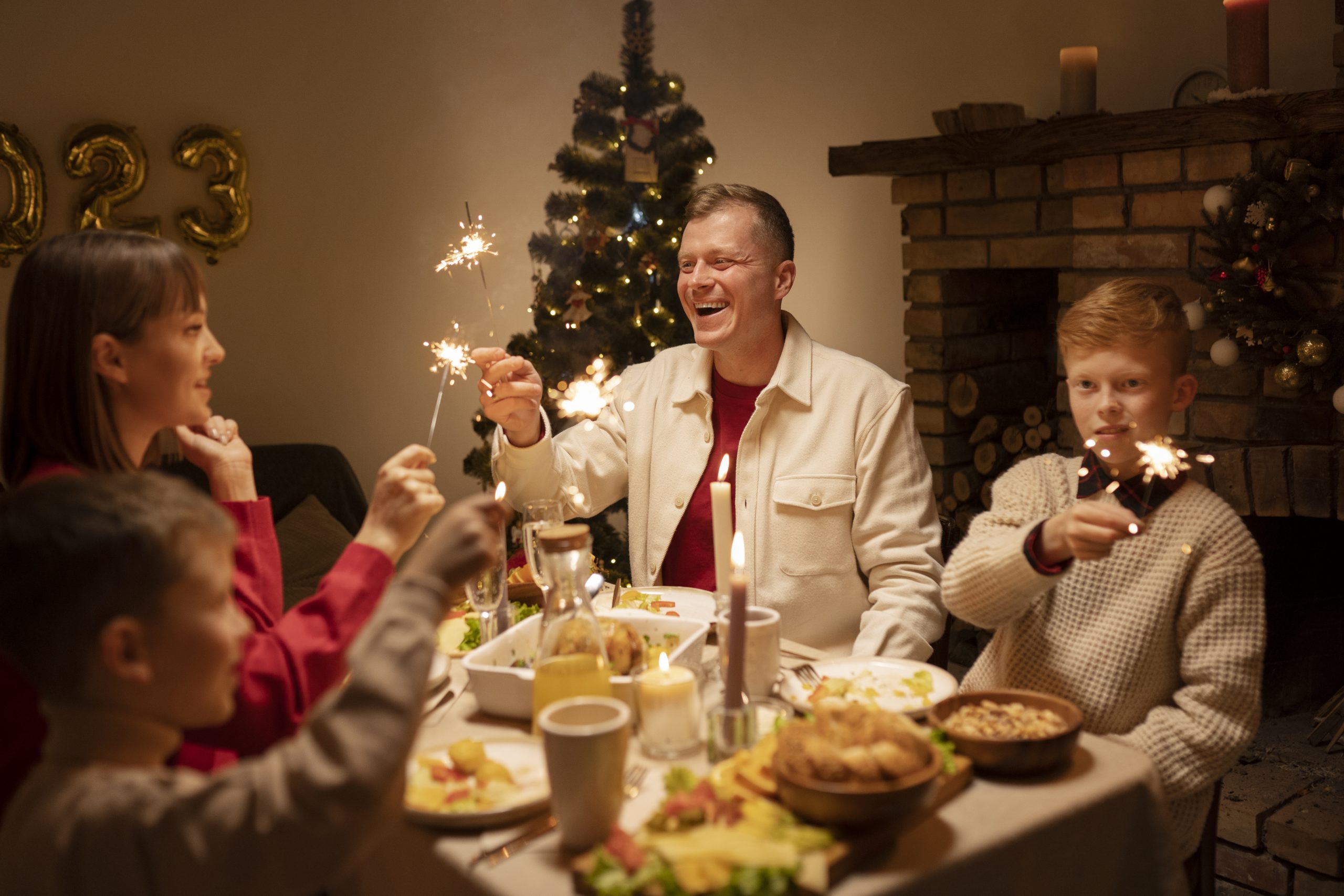 A joyful family celebrates with sparklers at a festive dinner table near a Christmas tree. 