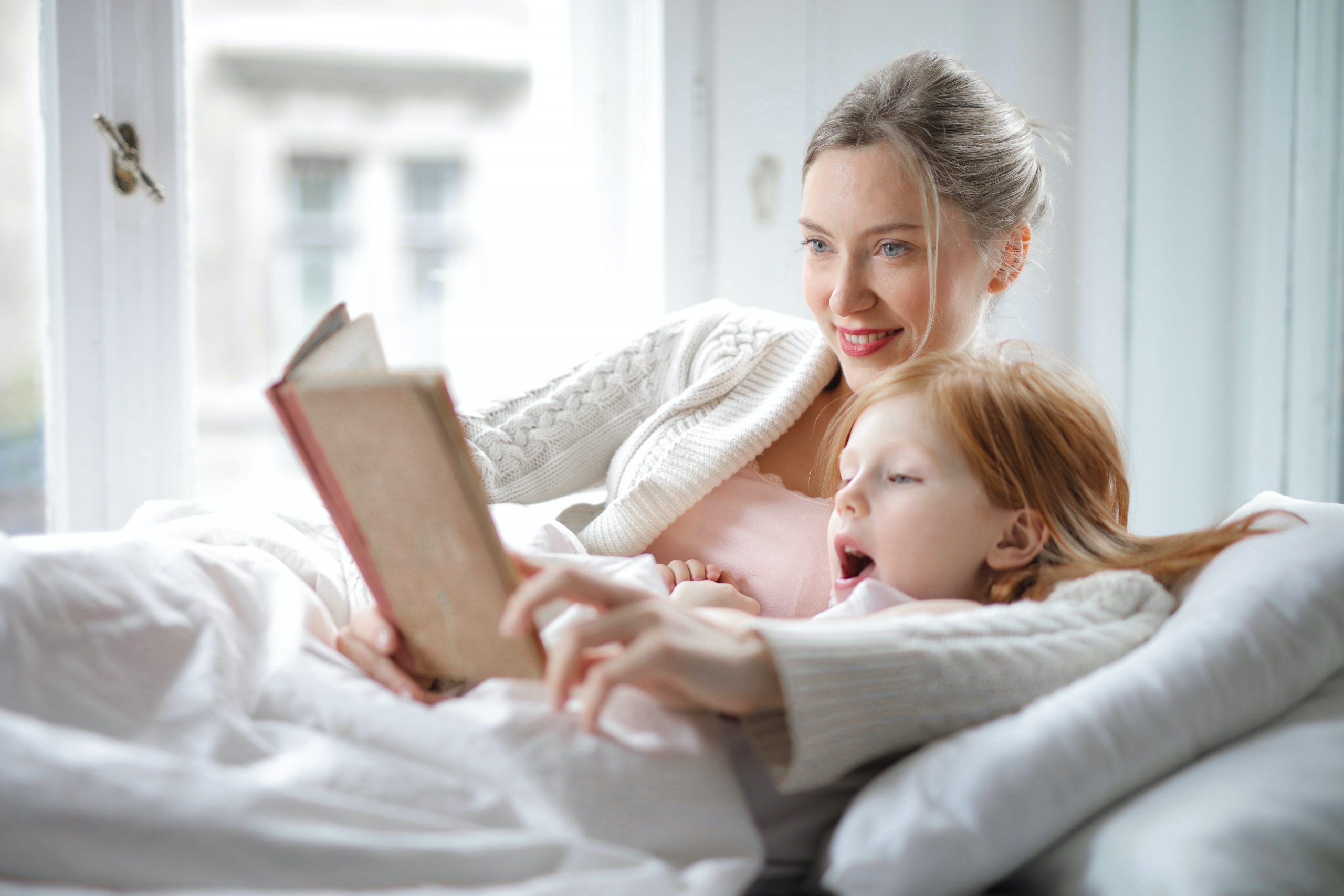A mother and daughter are reading a book while lying down