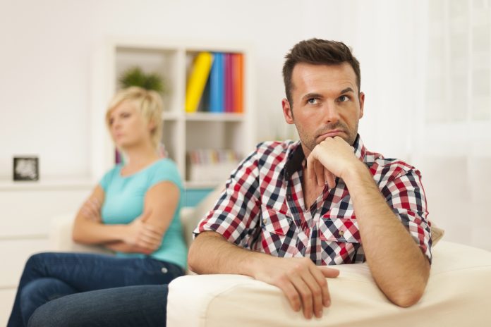 A mother and son sit apart with tense expressions, indicating relationship issues in a home setting.