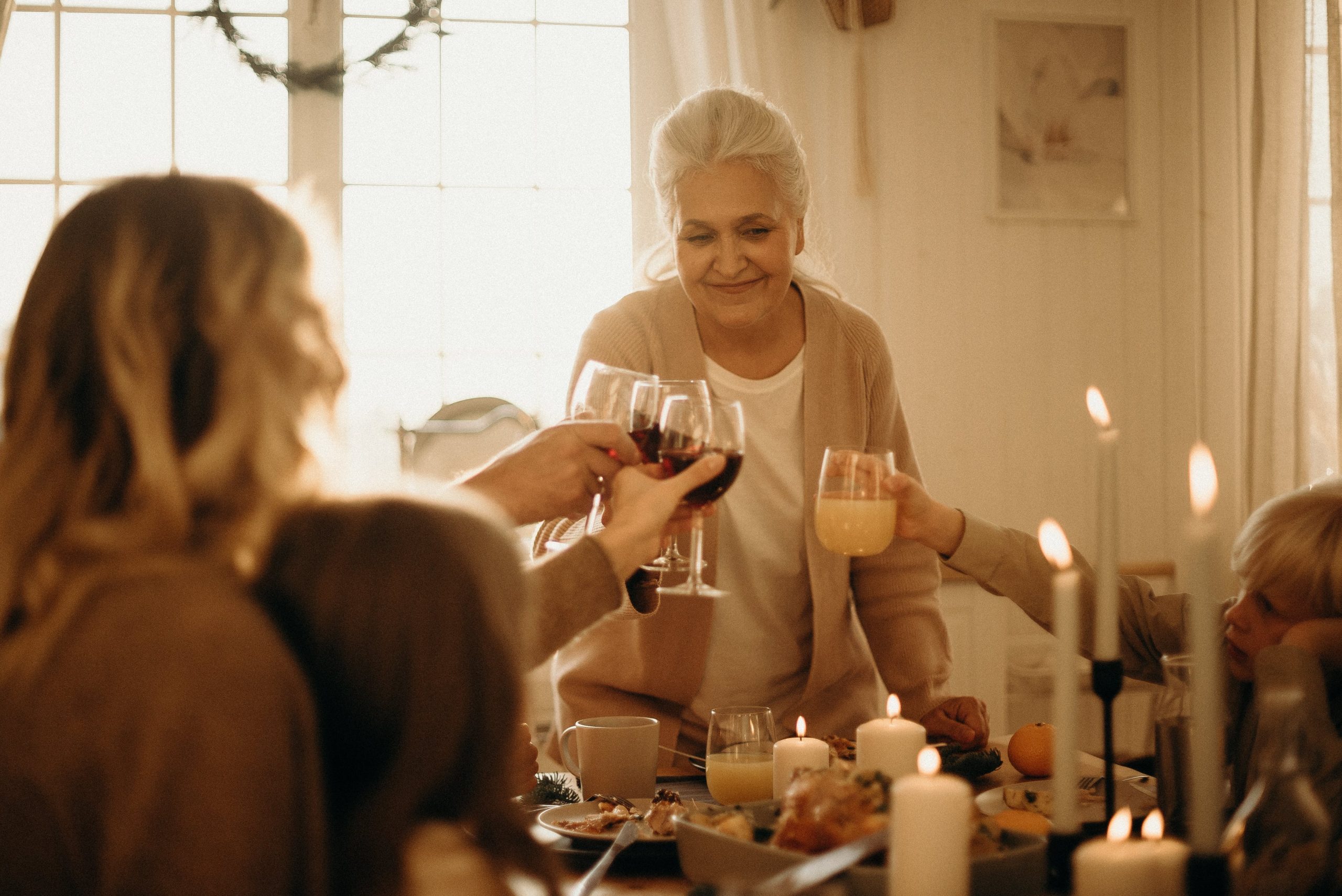 Elderly woman toasting with family during a warm, candlelit dinner gathering at home. 