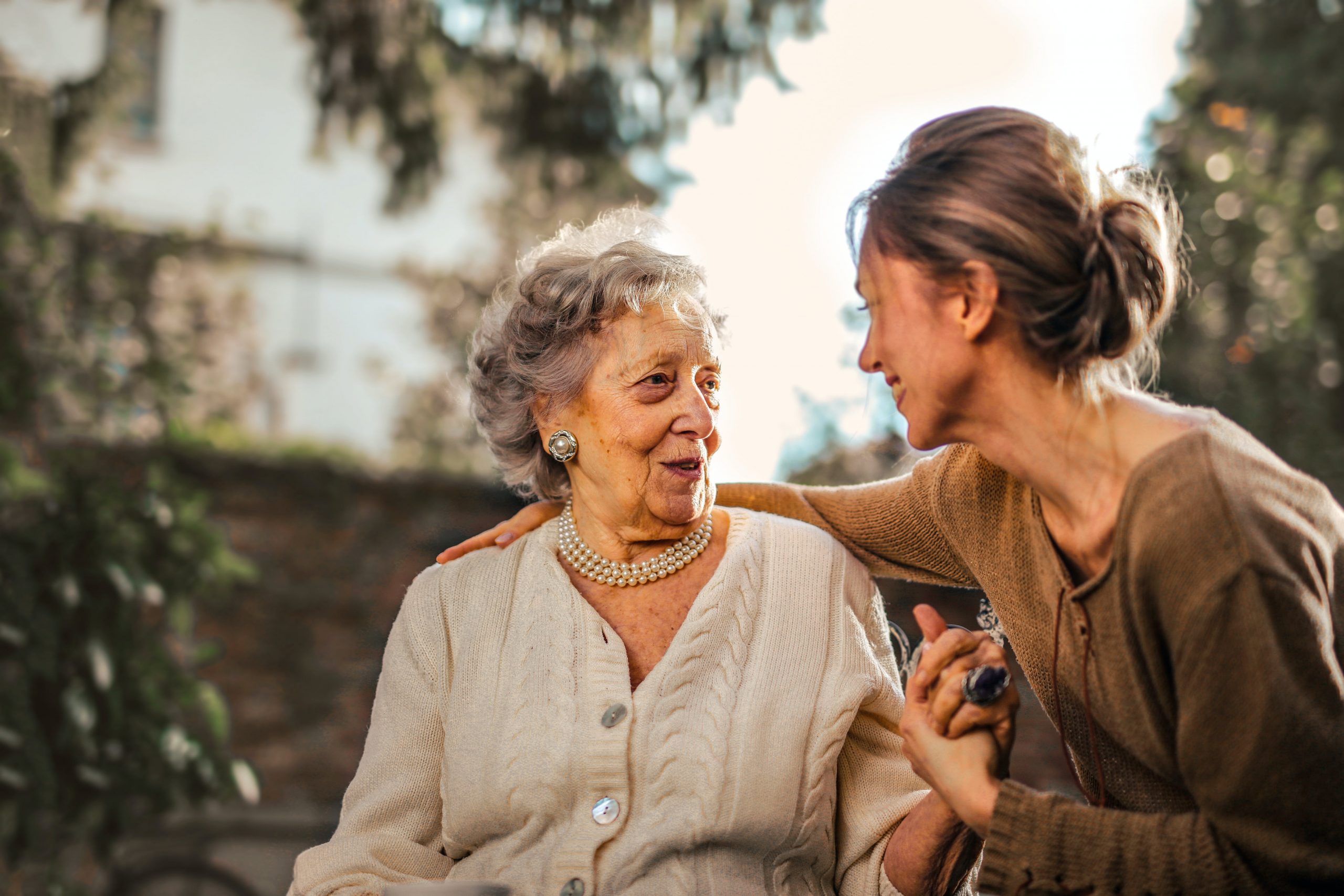 An elderly woman conversing and sharing a moment with a younger woman outdoors. 