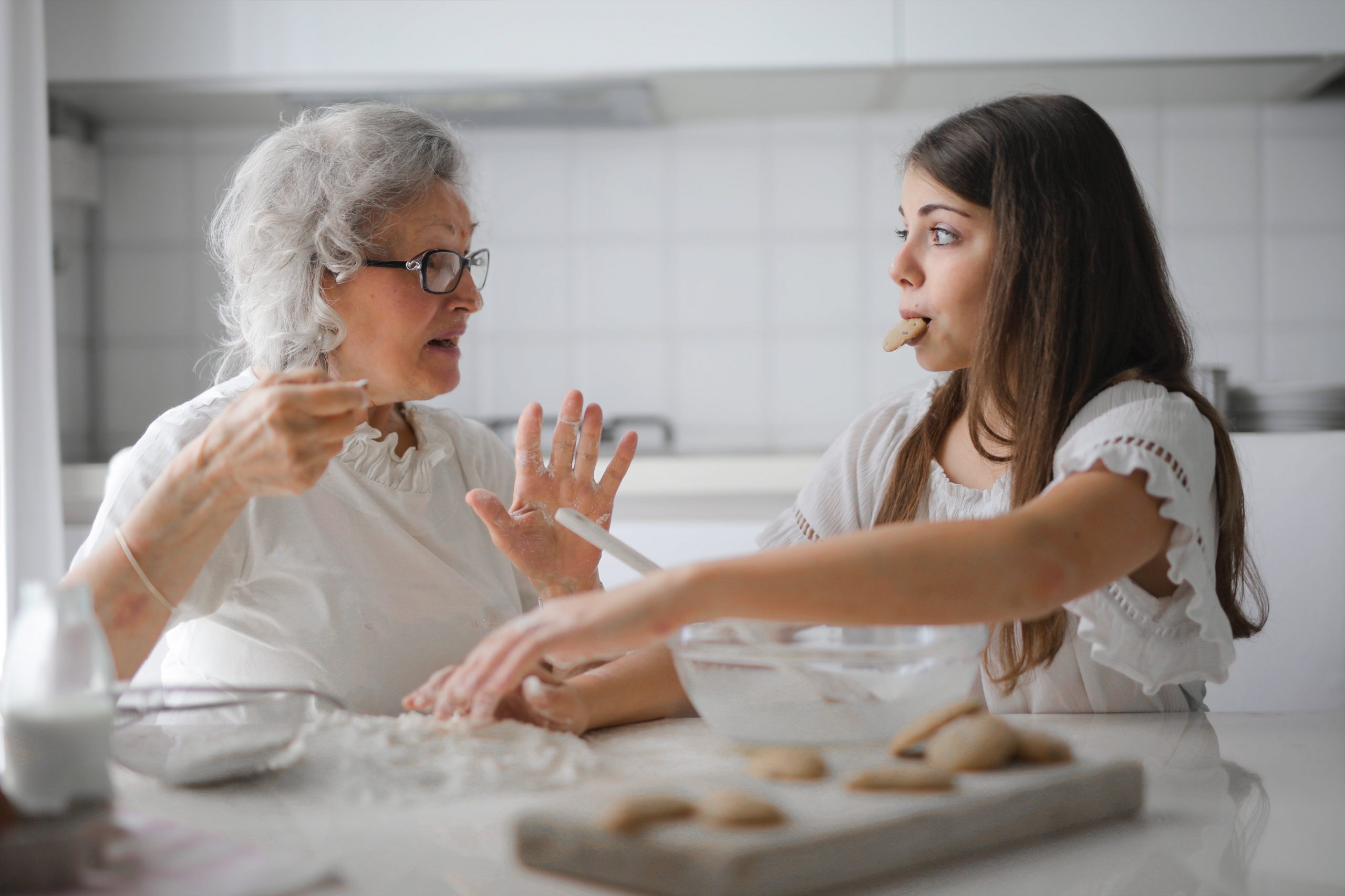 Grandmother and granddaughter baking together, talking and having fun in a bright kitchen. 