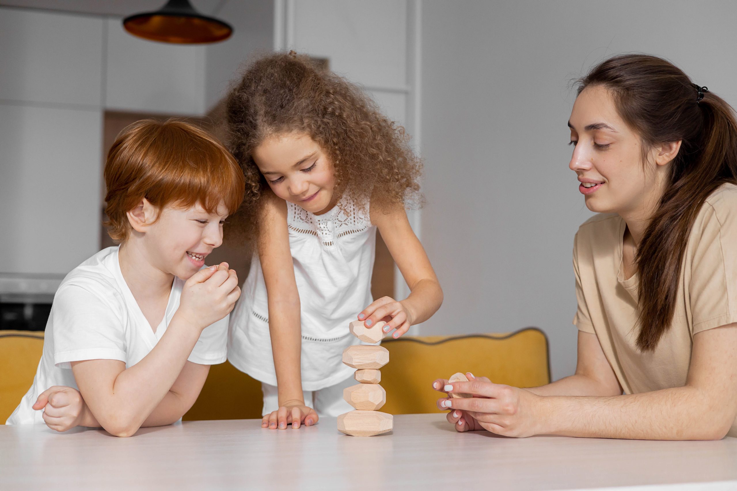 Two children and a young woman smiling and playing a stacking block game together. 