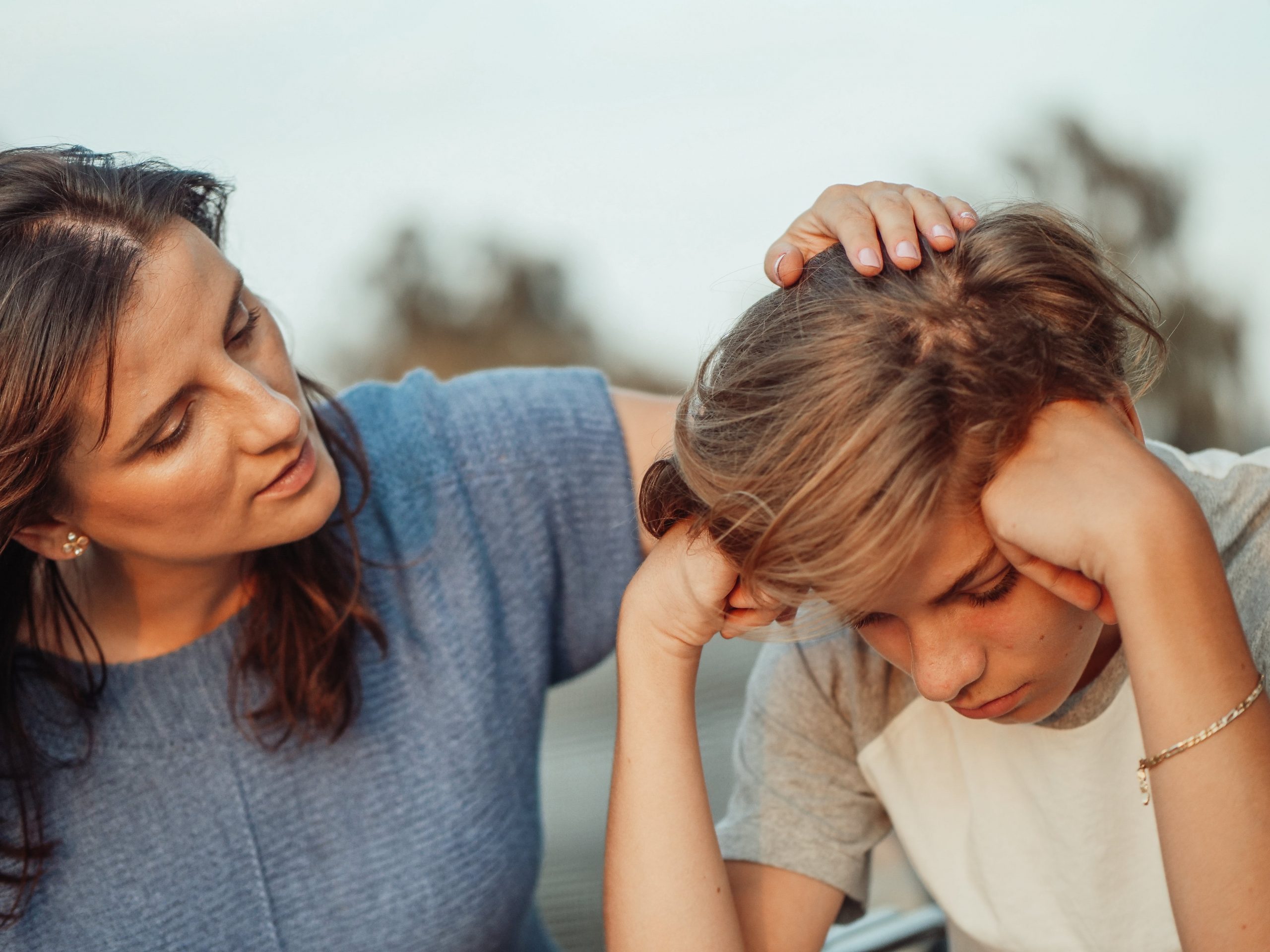 A woman comforting a distressed young boy outdoors, both showing expressions of concern and sadness.